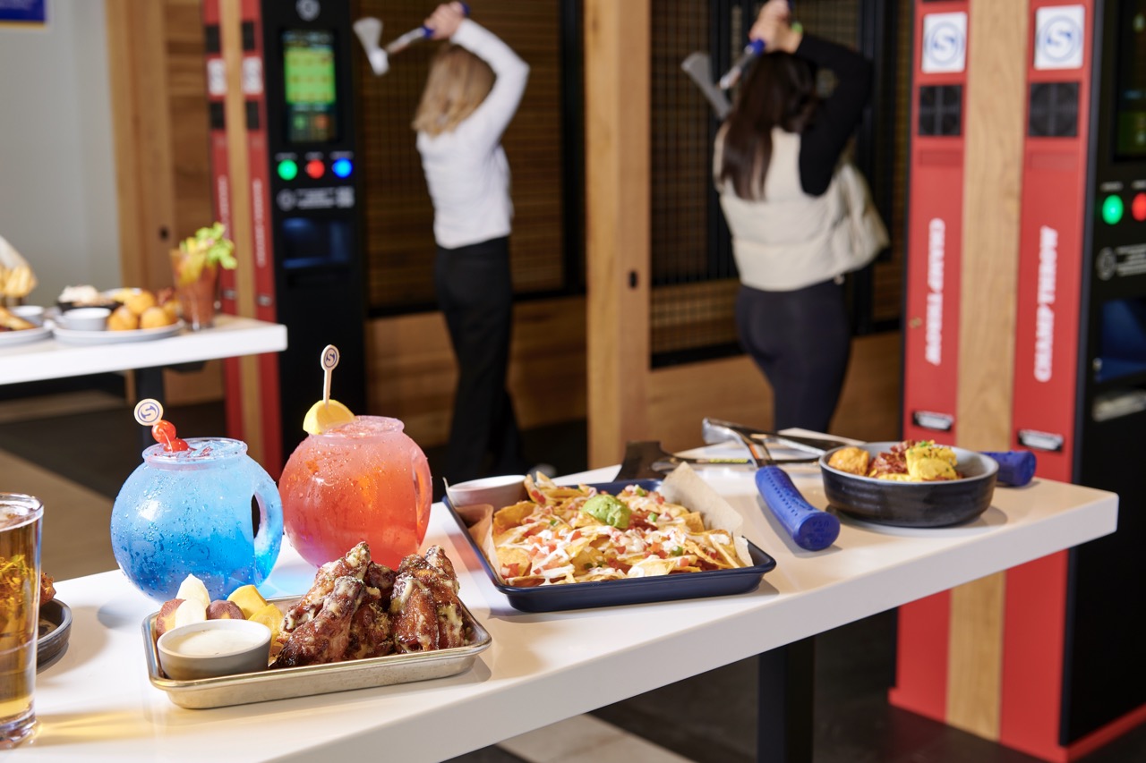 photo of a spread of food with two people throwing axes in the background